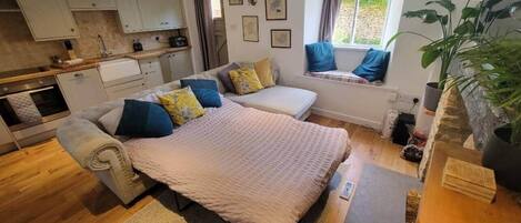 A cozy bedroom with a bed, a sofa, a window seat, and a kitchen area.