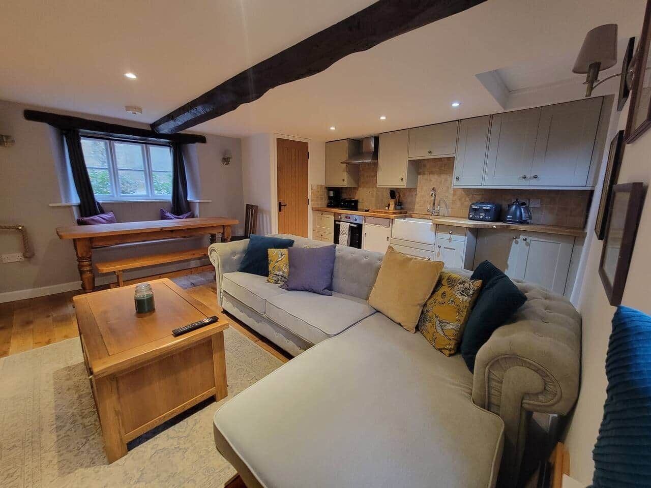 Una sala de estar acogedora con un sofá, una mesa de centro y un comedor con un banco. Se ve una cocina al fondo.