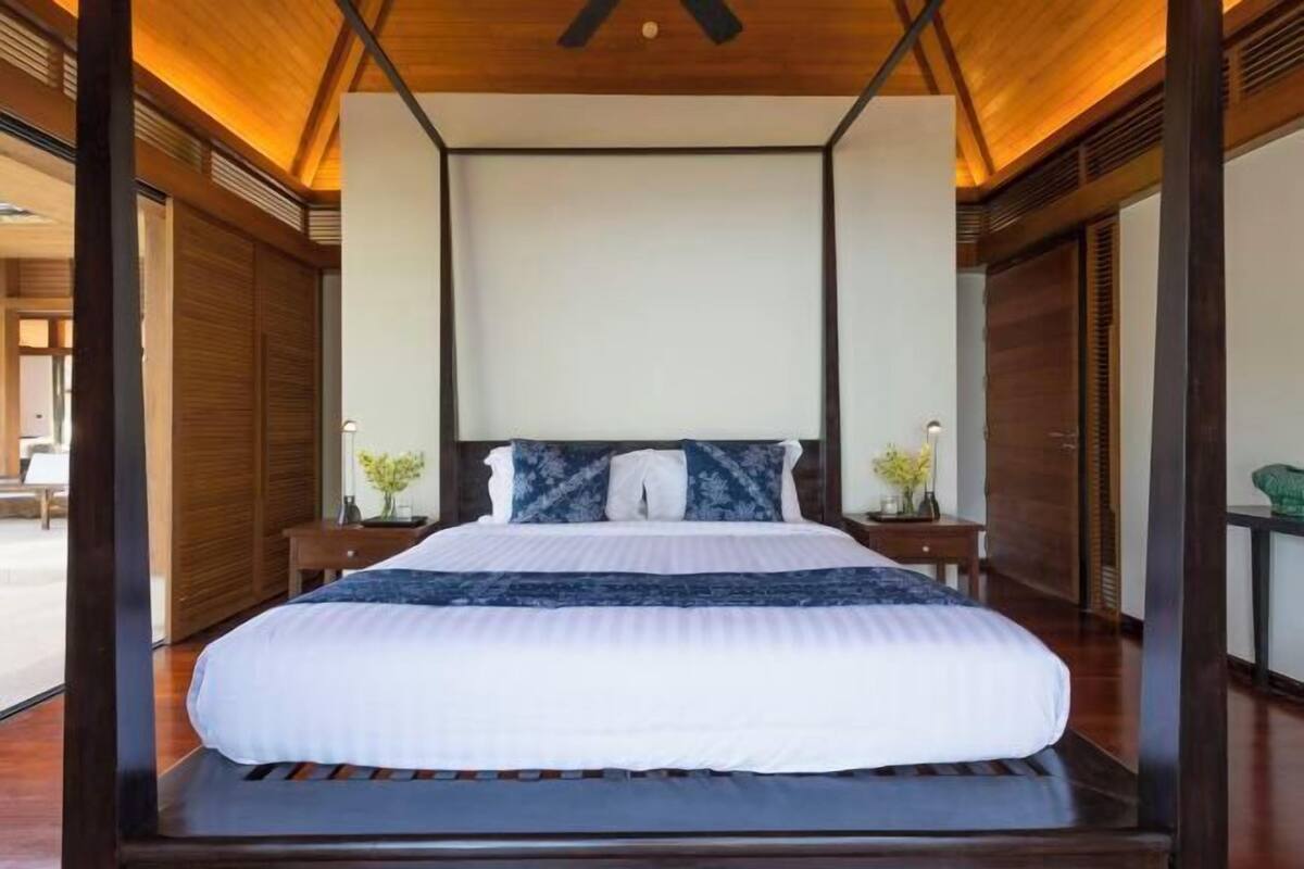 A centrally positioned bed with a canopy, flanked by wooden panels and a view of the outdoors.