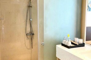 Un baño con ducha, lavamanos con artículos de aseo y un espejo.