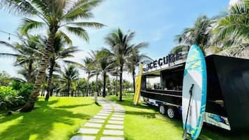 A pathway leading to a food truck with a surfboard, surrounded by palm trees.