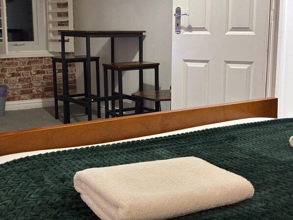 A room with a bed, a wooden chair, a small table, a brick wall, and a white door. - Loft 2bed Appartment with EVCharger (Portsmouth)