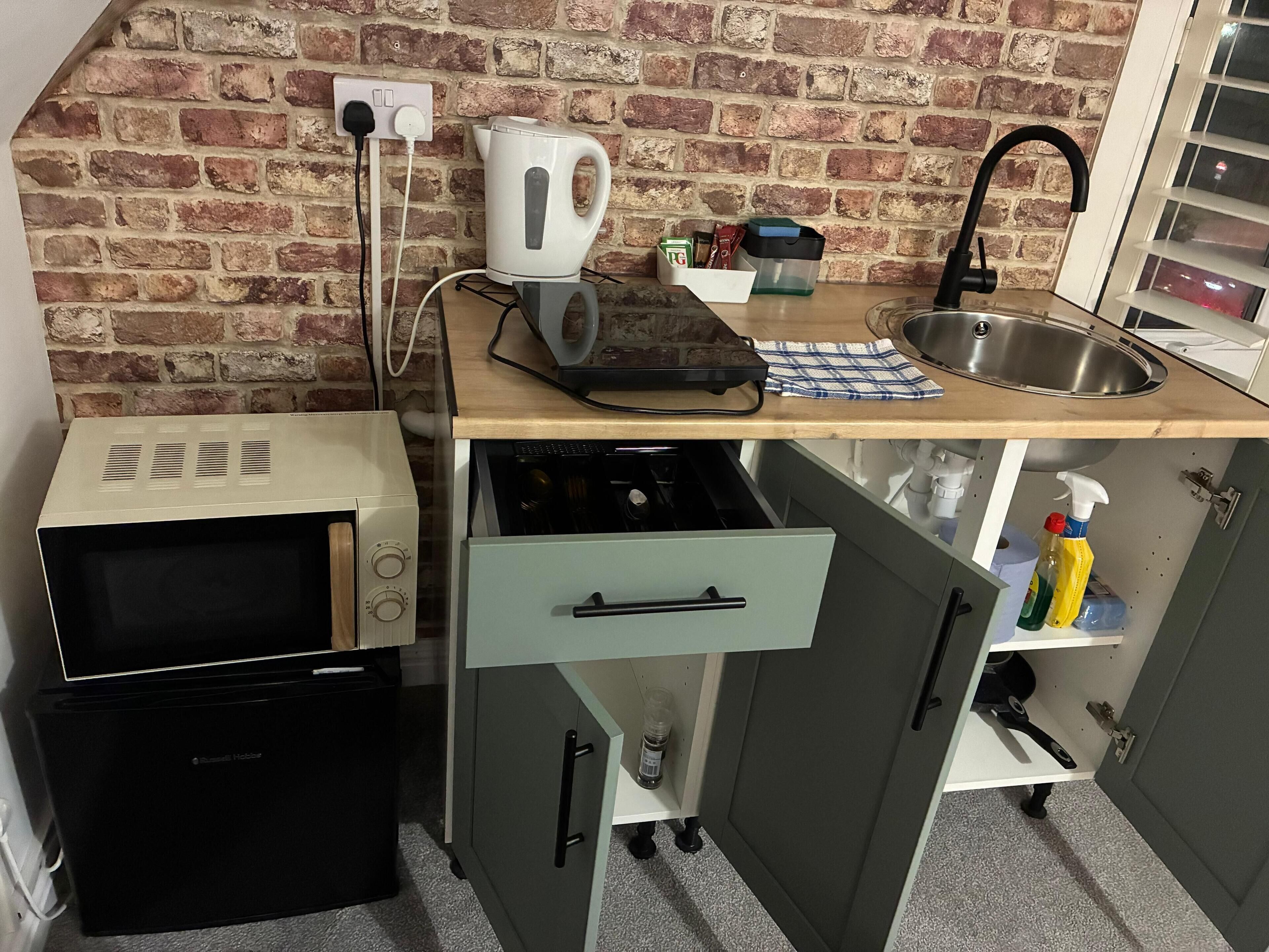 Una kitchenette compacta equipada con microondas, tostadora, hervidor de agua, pileta y alacenas.