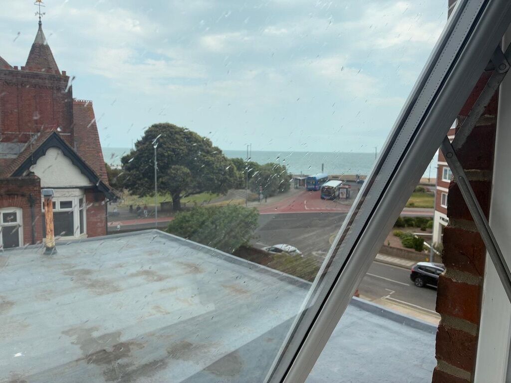 A view from a window overlooking a street with a church and a road leading to the sea.