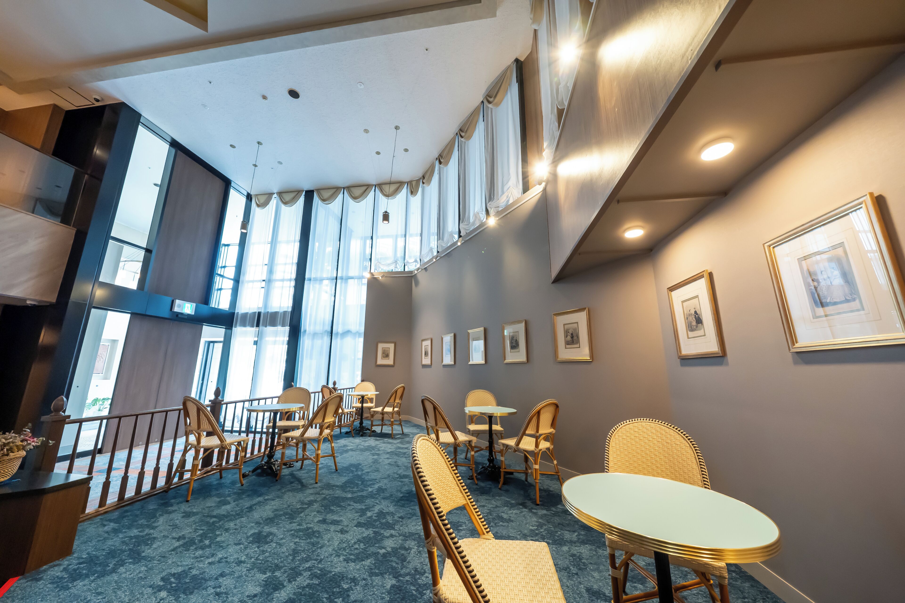 En hotellobby med högt i tak, stora fönster och en blå matta. Här finns flätade fåtöljer och bord som är placerade för gästernas bekvämlighet.