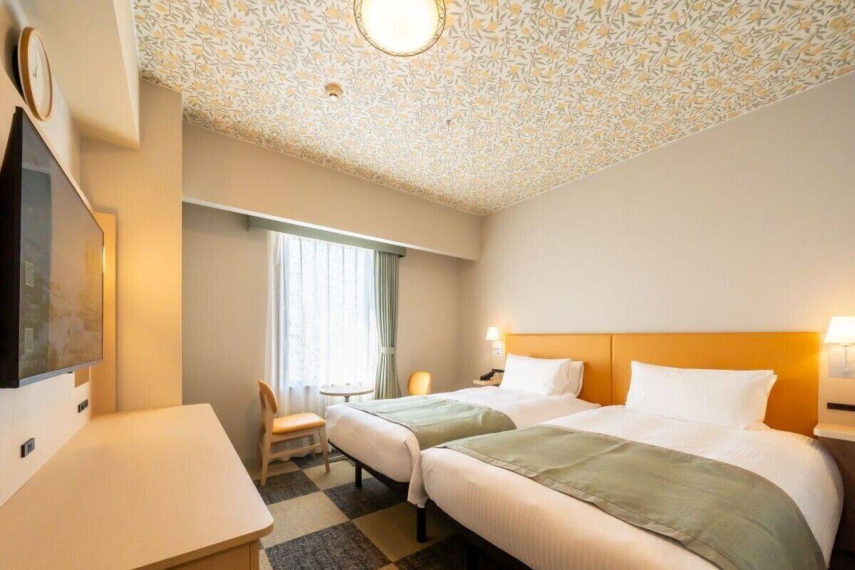 Habitación de hotel con dos camas, un escritorio, una silla, un televisor y techo con diseño.