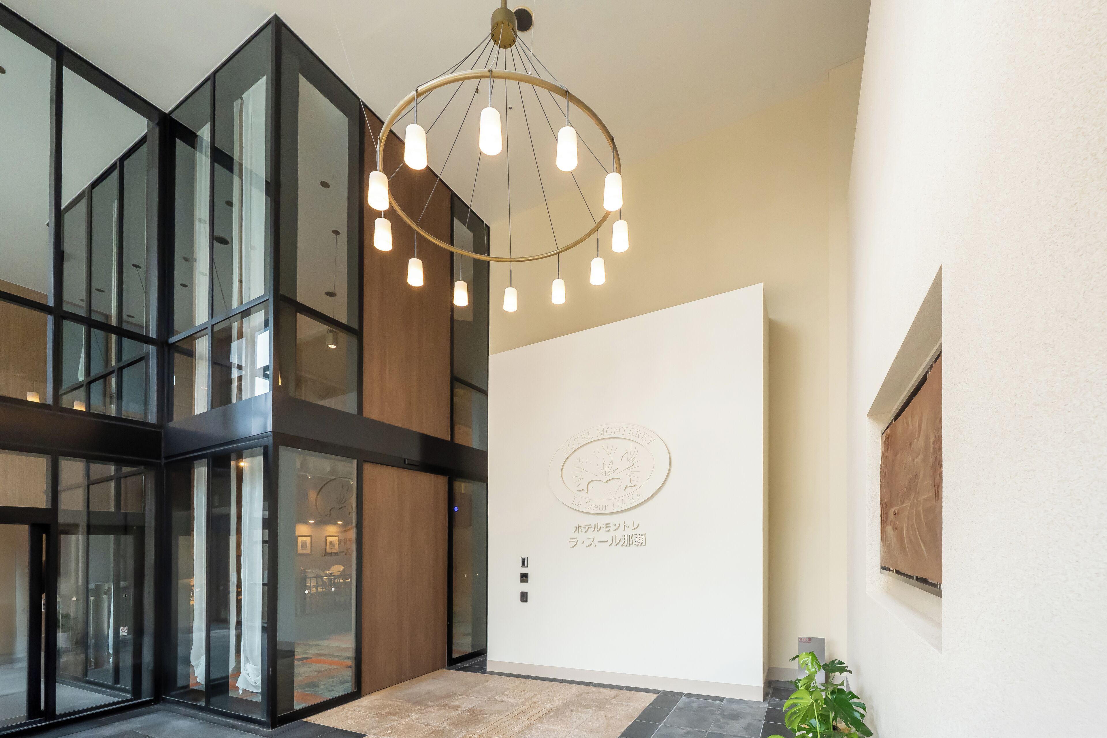 A modern hotel lobby with a glass partition, a wooden reception desk, and a ceiling light fixture.