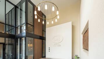 A modern hotel lobby with a glass partition, a wooden reception desk, and a ceiling light fixture.