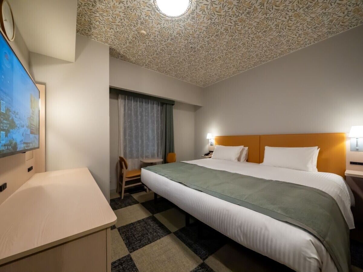 Habitación de hotel con cama, escritorio, silla, televisión y techo estampado.