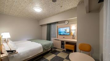 A hotel room with a bed, a desk with a computer, a chair, a small table, and a television.
