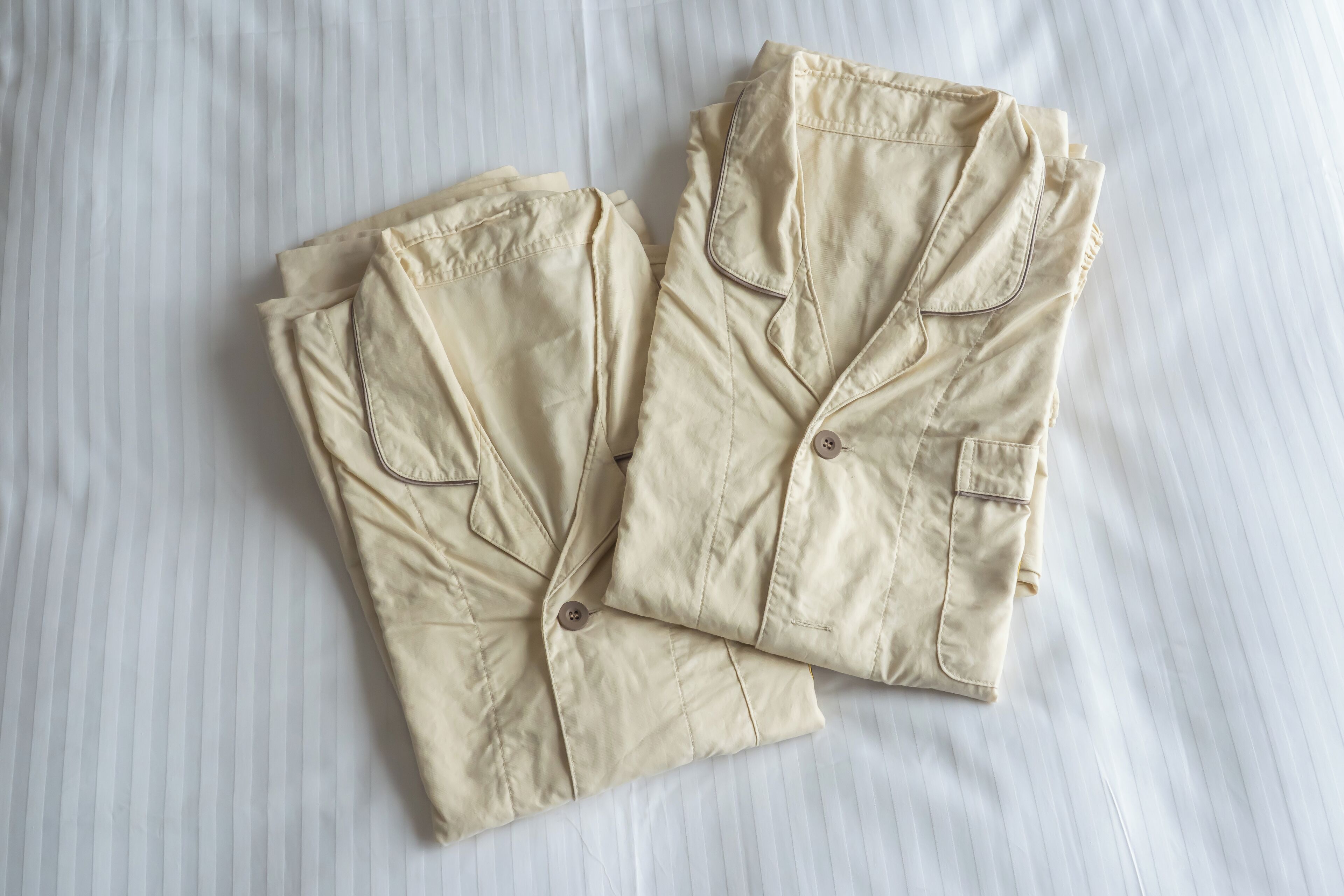 Two beige shirts with buttons and pockets, laid out on a white surface.