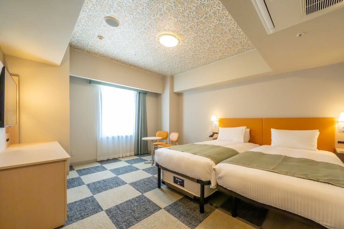 Habitación de hotel con dos camas, un escritorio, una silla, una mesita y una ventana con cortinas.