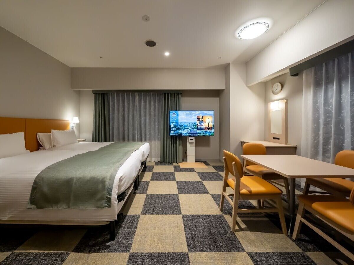 A hotel room with a bed, a TV, a desk, and a chair.