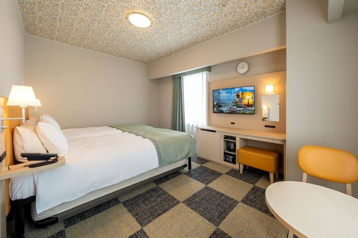Habitación de hotel con cama, escritorio, silla, televisión y techo estampado.