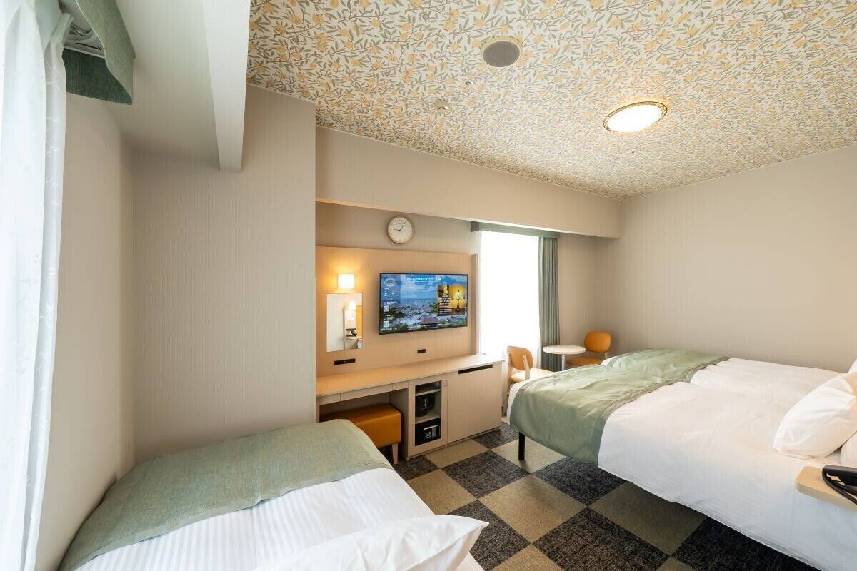 Una habitación de hotel con dos camas, un escritorio, un televisor y un reloj en la pared.