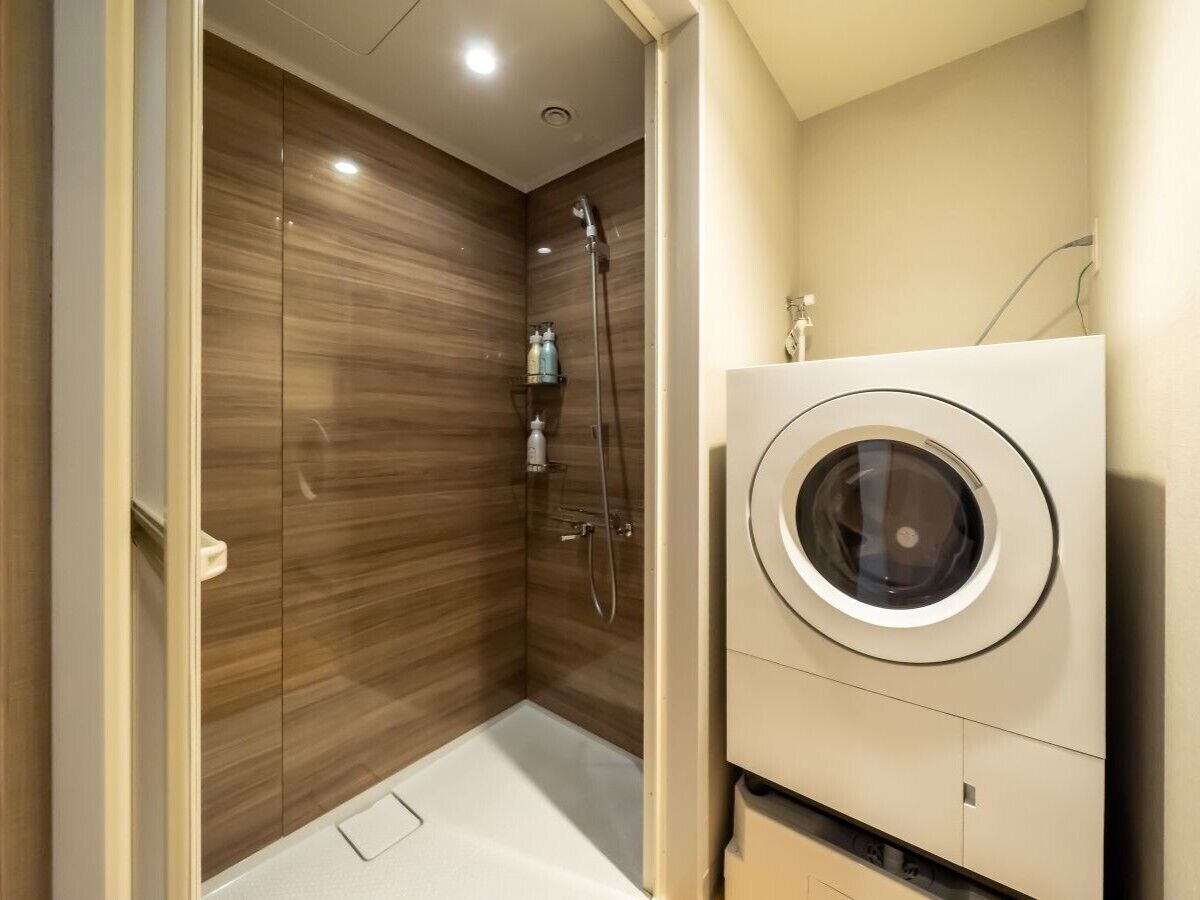 A compact bathroom with a shower, a built-in washing machine, and wooden paneling.