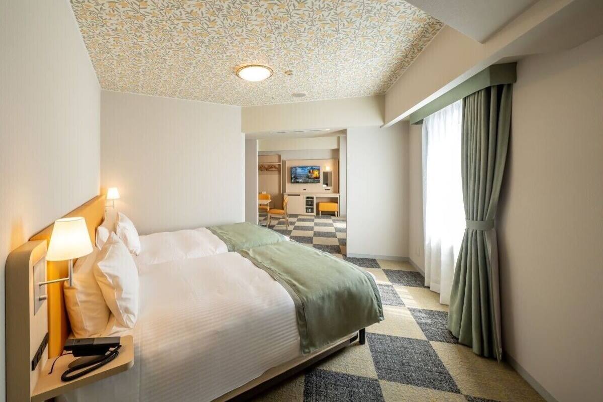 Habitación de hotel con cama, escritorio, televisión y techo con diseño.