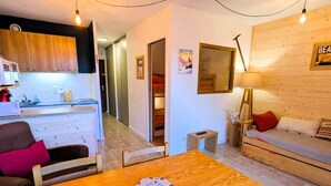 A cozy living room with a wooden table, a sofa, and a small side table. There is a kitchen area with cabinets and a microwave visible in the background. - Large studio cabin 4 pers. with garage 600m from ski lifts (Arêches-Beaufort)