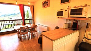 A small kitchen with a wooden table and chairs, a window with a view of the countryside, and a microwave oven. - Large studio cabin 4 pers. with garage 600m from ski lifts (Arêches-Beaufort)