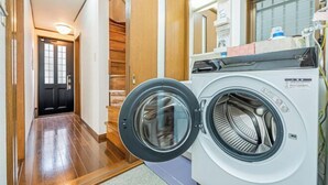 Un lavadero con una lavadora de carga frontal, una puerta de madera y un pasillo que lleva a una puerta negra.