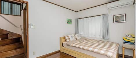 A bedroom with a bed, a window with curtains, a small table with a chair, and a staircase.