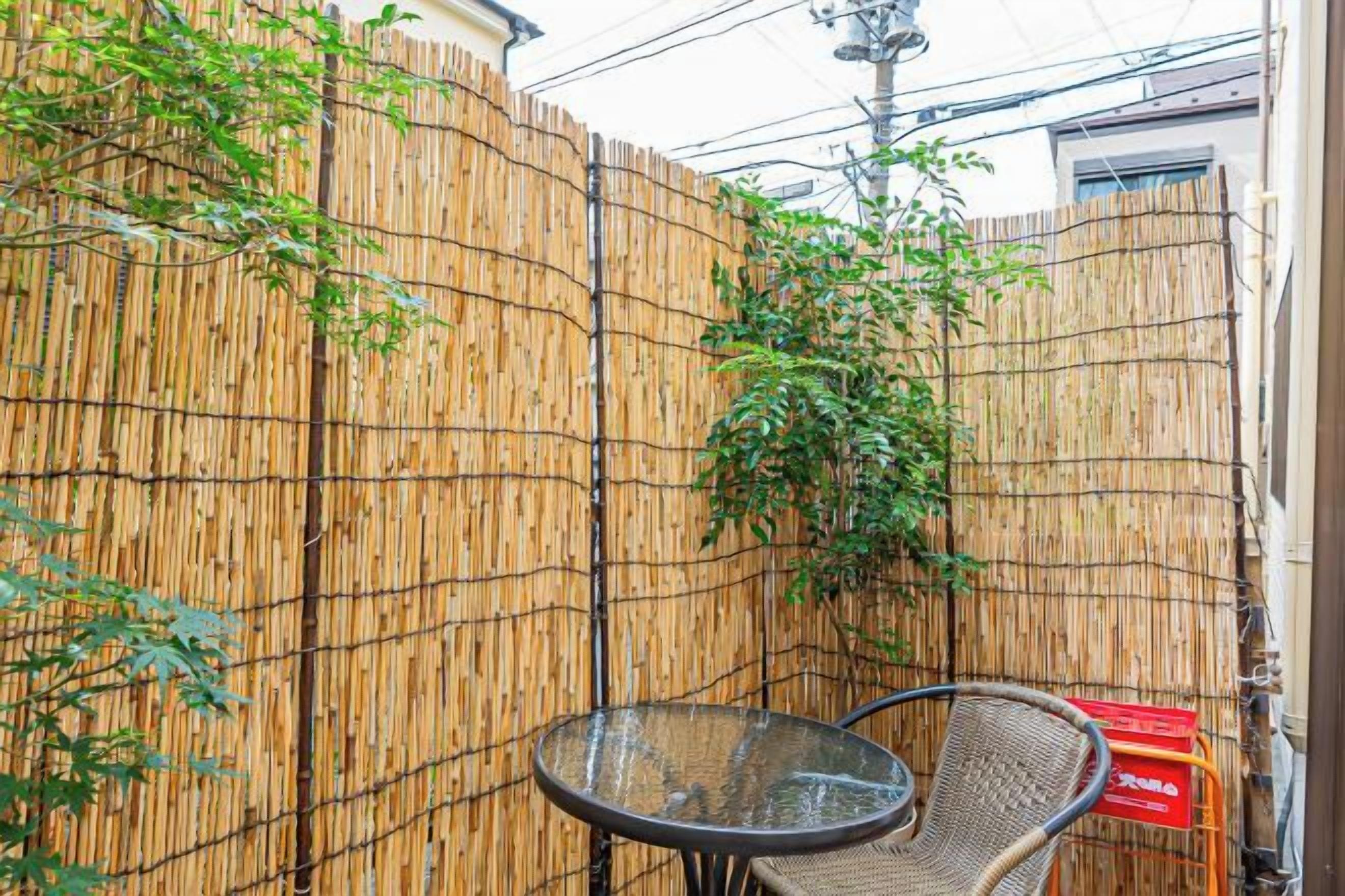 A bamboo fence, a glass table, and a wicker chair in a courtyard.