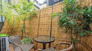 Un área exterior con asientos de mimbre, una mesa de vidrio, cerca de bambú y una planta en maceta.