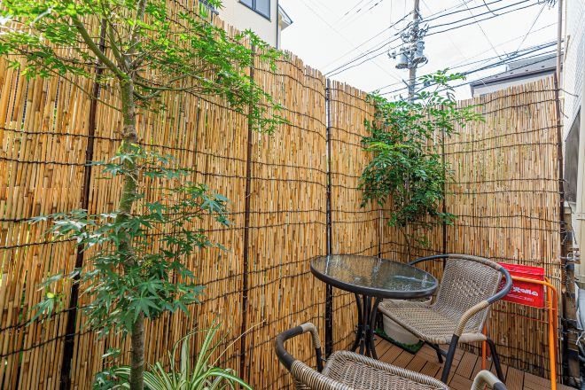 A bamboo fence, a round table, and wicker chairs in a courtyard.
