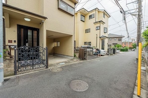 A residential street with a beige building, a black gate, and a person walking.