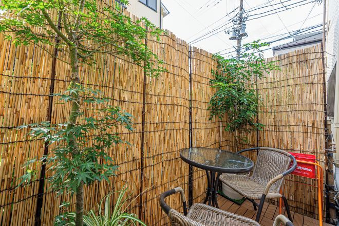 A bamboo fence, two wicker chairs, and a glass table in an outdoor area.