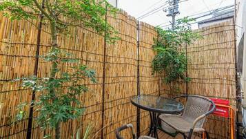 A bamboo fence, two wicker chairs, and a glass table in an outdoor area.