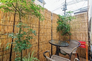 A bamboo fence, two wicker chairs, and a glass table in an outdoor area.