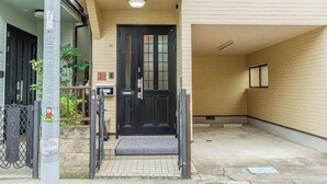 Entrada de un edificio con una puerta negra, un pequeño porche y suelo de baldosas.