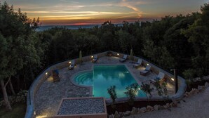 A pool area with lounge chairs and a stone deck, surrounded by trees. - Villa Ana, Spacious 5 Bedroom Retreat with Access to 2 Shared Pools (Koromačno)