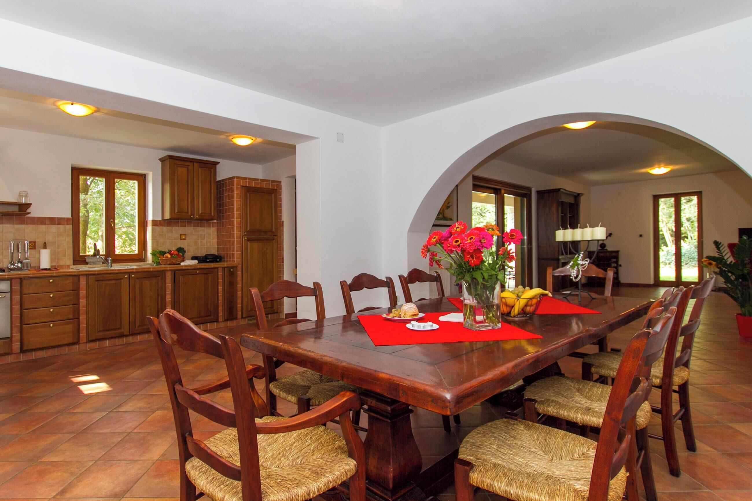 A spacious dining area with a large wooden table, surrounded by wicker chairs, and a red placemat.