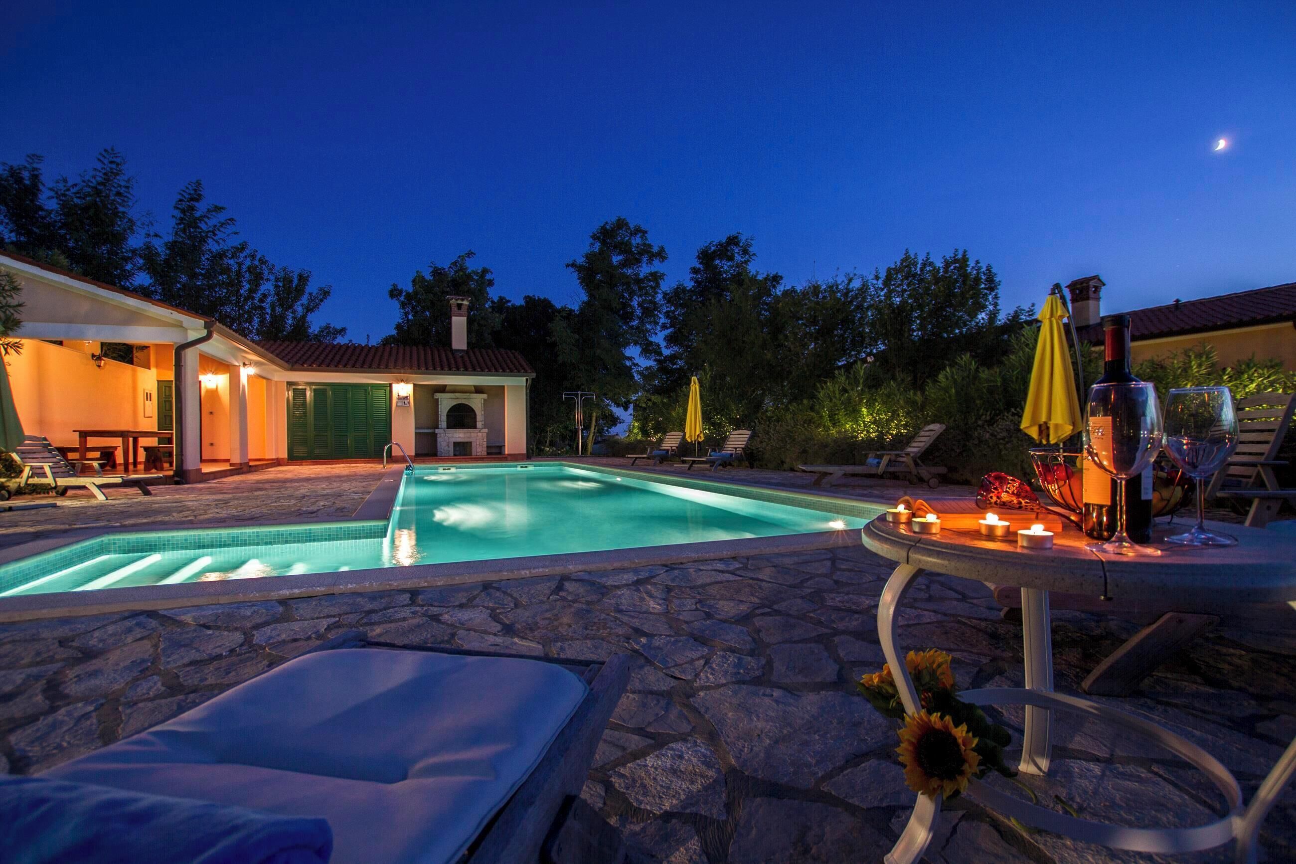 Ein Swimmingpool mit Liegestühlen, einem Tisch mit Kerzen und Blick auf einen Sonnenuntergang.