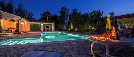 Ein Swimmingpool mit Liegestühlen, einem Tisch mit Kerzen und Blick auf einen Sonnenuntergang.