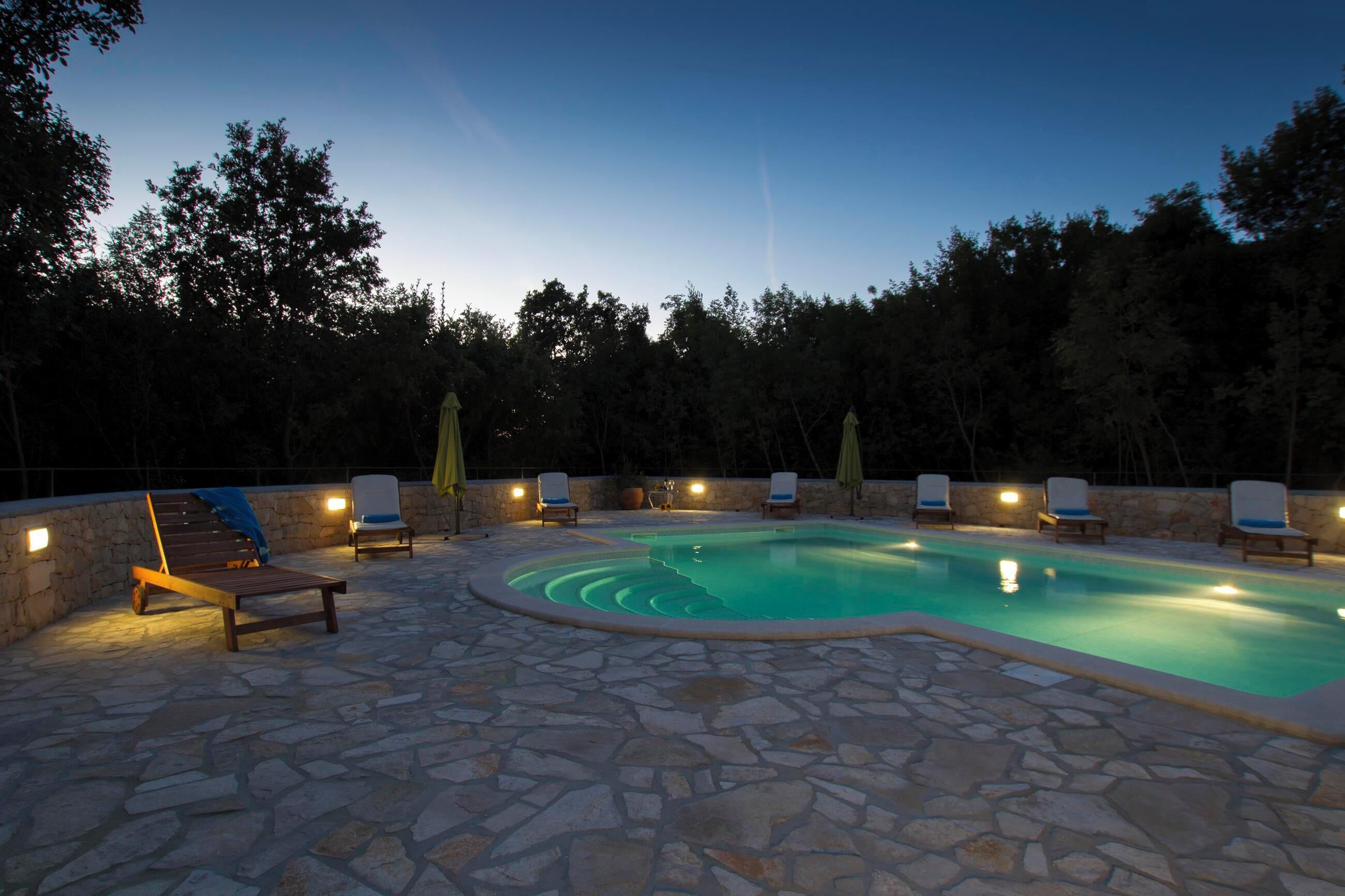 A swimming pool with stone flooring and lounge chairs.