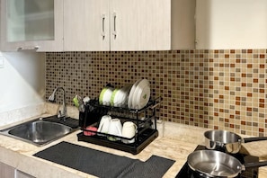 A kitchen with a tiled backsplash, a dish rack, a sink, and a stove. - Strategic MTH Square Apt 1BR w/ Pool & Gym (East Jakarta)