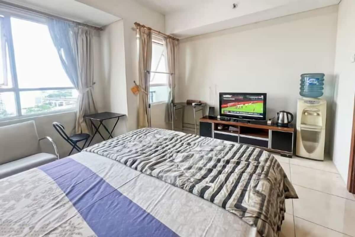 A hotel room with a bed, a television, a water dispenser, and a window with curtains.