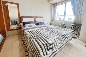 A bedroom with a bed, a bedside table, a chair, a window with curtains, and a mirror on the wall. - Strategic MTH Square Apt 1BR w/ Pool & Gym (East Jakarta)