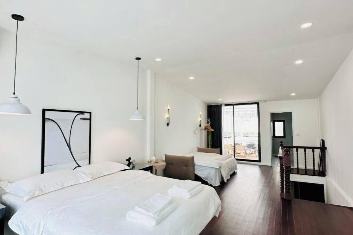 A hotel room with two beds, a desk, a chair, a staircase, and a view of the outside.