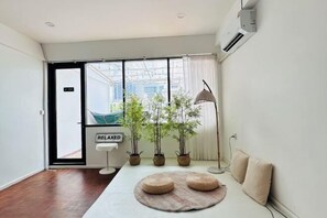 Une chambre moderne avec une grande fenêtre, un canapé, une table ronde avec un set de table et des plantes en pot.