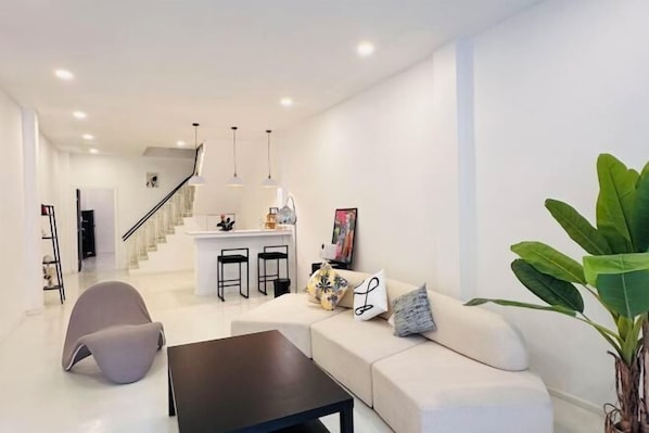 A modern living room with a sofa, a coffee table, and a chair. There is a staircase leading to an upper level.
