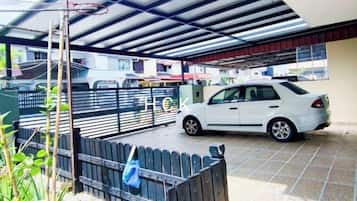 Uma área de estacionamento coberta com um carro branco estacionado, uma cerca de metal e um edifício ao fundo.