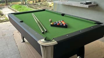 A pool table with balls and cues, a window, and a small shelf with items.