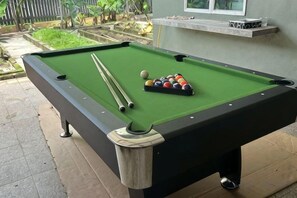 A pool table with balls and cues, a window, and a small shelf with items. - Lovely Garden Home BBQ Event at Klang by HCK (Klang District)