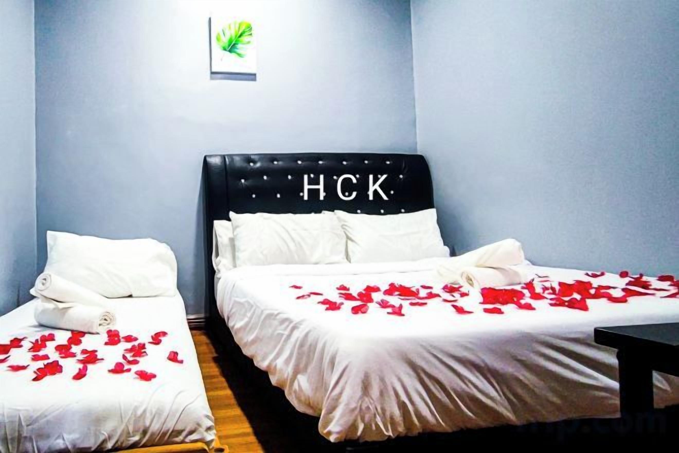 Een hotelkamer met twee bedden, waarvan één een hoofdeinde heeft met 'HCK' en de ander een egaal hoofdeinde. Beide bedden zijn voorzien van witte lakens en kussens.