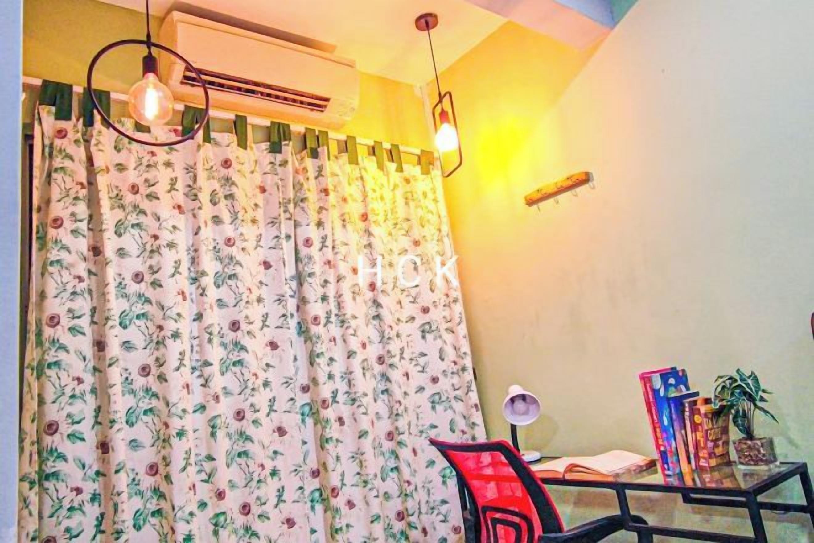 A room with a bed, a desk with a chair, a potted plant, and a window with curtains.