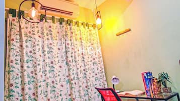 A room with a bed, a desk with a chair, a potted plant, and a window with curtains.